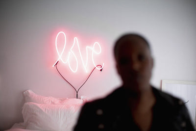 Enseigne au néon LOVE au-dessus d'un lit avec une personne au premier plan